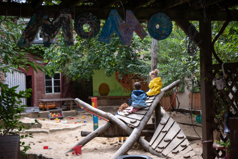 Zwei Kinder sitzen auf dem großen Spielgerüst im Sandkasten des MOMO-Hofes