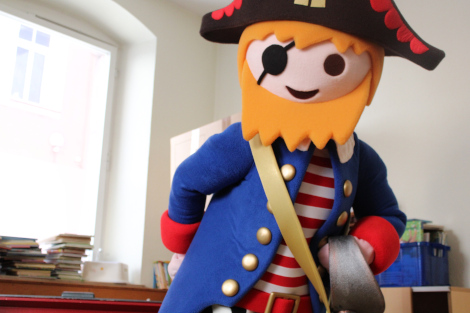 Im Bild ist eine Person im Kostüm eines Playmobil-Piraten zu sehen, mit Dreispitz, Augenklappe und einem blauen Mantel. 