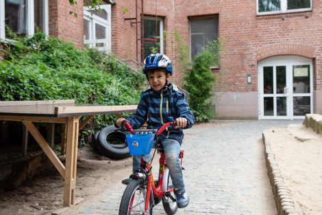 Ein Kind fährt auf einem Fahrrad auf dem Weg zur MOMO-Eingangstür