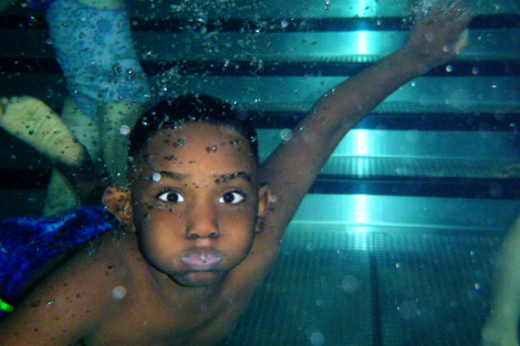 Ein Junge unter Wasser schaut mit aufgeplasenen Backen in die Kamera.
