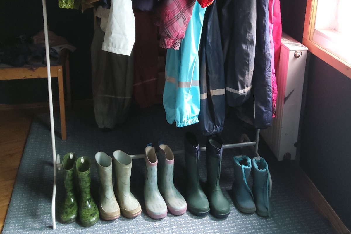 Eine Auswahl der aussortierten Kleider auf einem Kleiderständer und Gummistiefel, die davor stehen.