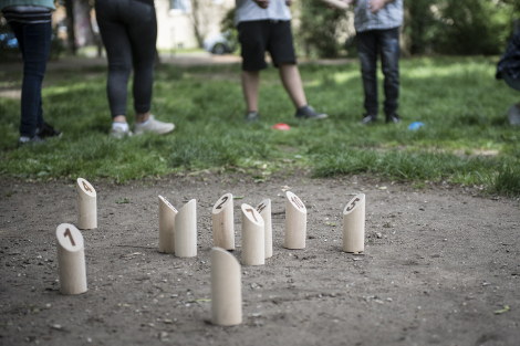 In einer Grünanlage stehen mehr als 10 Holzklötzchen von dem Spiel Mölky. Im HIntergrund sind die Beine von Menschen zu sehen.