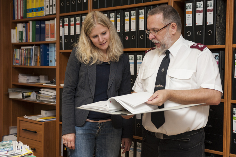 Eine blonde Frau und ein Mann mit weißem Uniformhemd blicken gemeinsam in einen ordner.