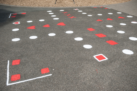 Auf einem geteerten Platz ist mit roten und weißen Punkten ein großes Spielfeld für Mensch-ärgere-Dich-nicht aufgemalt.