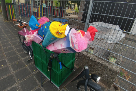 Transportrad mit bunten Schultüten in grünen Kisten steht vor dem Zaun einer Kindertagesstätte.