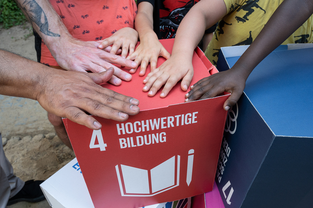 Viele Hände über einer Box mit der Aufschrift: Hochwertige Bildung.