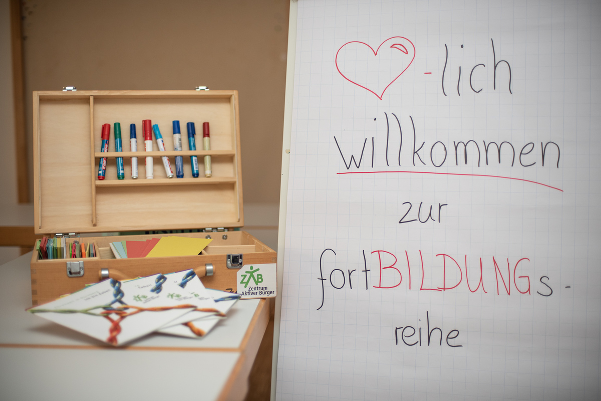 Flipchart mit Willkommensgruß zur einer Fortbildung, links daneben ein geöffneter Moderationskoffer