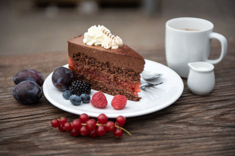 Ein Stück Schokoladenkuchen mit Obstgarnitur und eine Tasse Kaffee sind auf einem Tisch angerichtet.