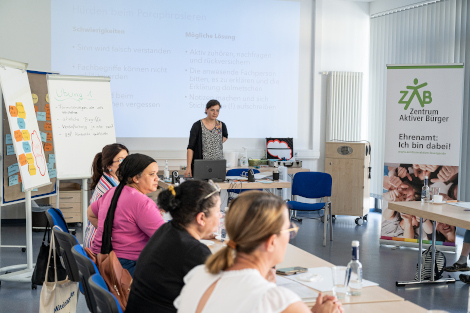 Eine Referentin steht vor den Sprachvermittlerinnen, die an Tischen sitzen