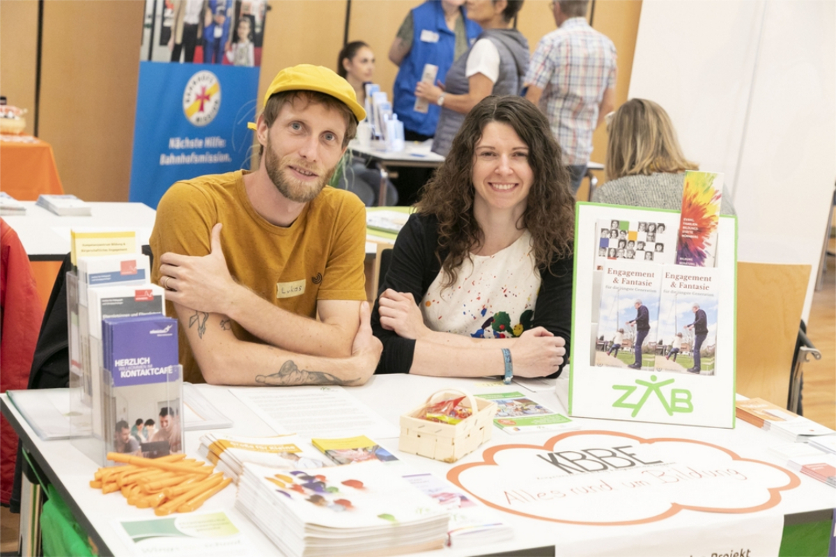 Lukas Binder und Betti Schiebel vom ZAB sitzen an einem Info-Tisch auf der Freiwilligenmesse 2023