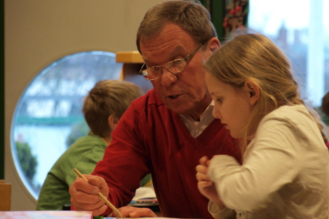 Ehrenamtlicher sitzt mit Kind am Tisch und hilft bei den Hausaufgaben