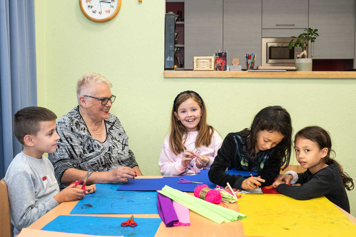 Ehrenamtlicher sitzt mit Kind am Tisch und hilft bei den Hausaufgaben