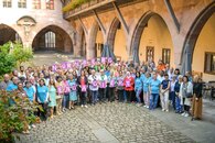 Eine große Gruppe von Menschen steht in einem Innenhof mit Säulen und blickt in die Kamera. Einige halten Schilder mit Buchstaben hoch, die folgenden Slogan bilden: Nürnberg engagiert