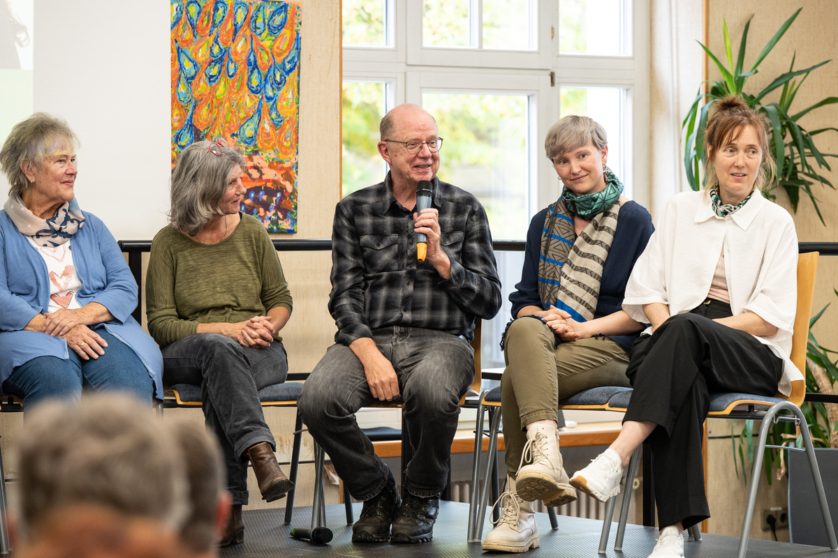 5 Personen sitzen auf Stühlen auf einer Bühne