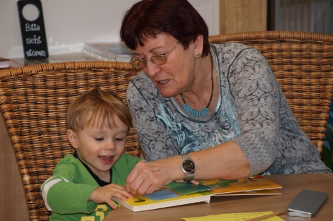 Ehrenamtliche Marianne Lechner sitzt beim Vorlesen im Kindergarten mit Kind am Tisch