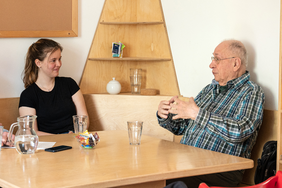 Die Freiwilligen Karl-Dieter Wilhelm und Maya Netter sitzen an einem Tisch und unterhalten sich.