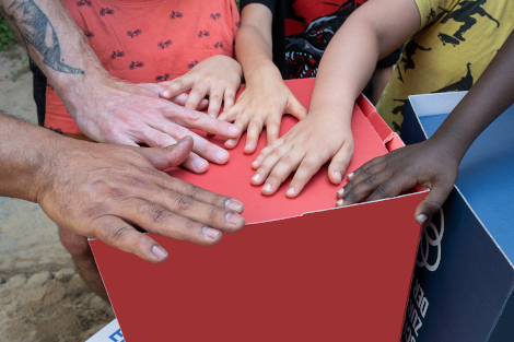 Hände mit verschiedenen Hautfarben liegen auf einer roten Box.