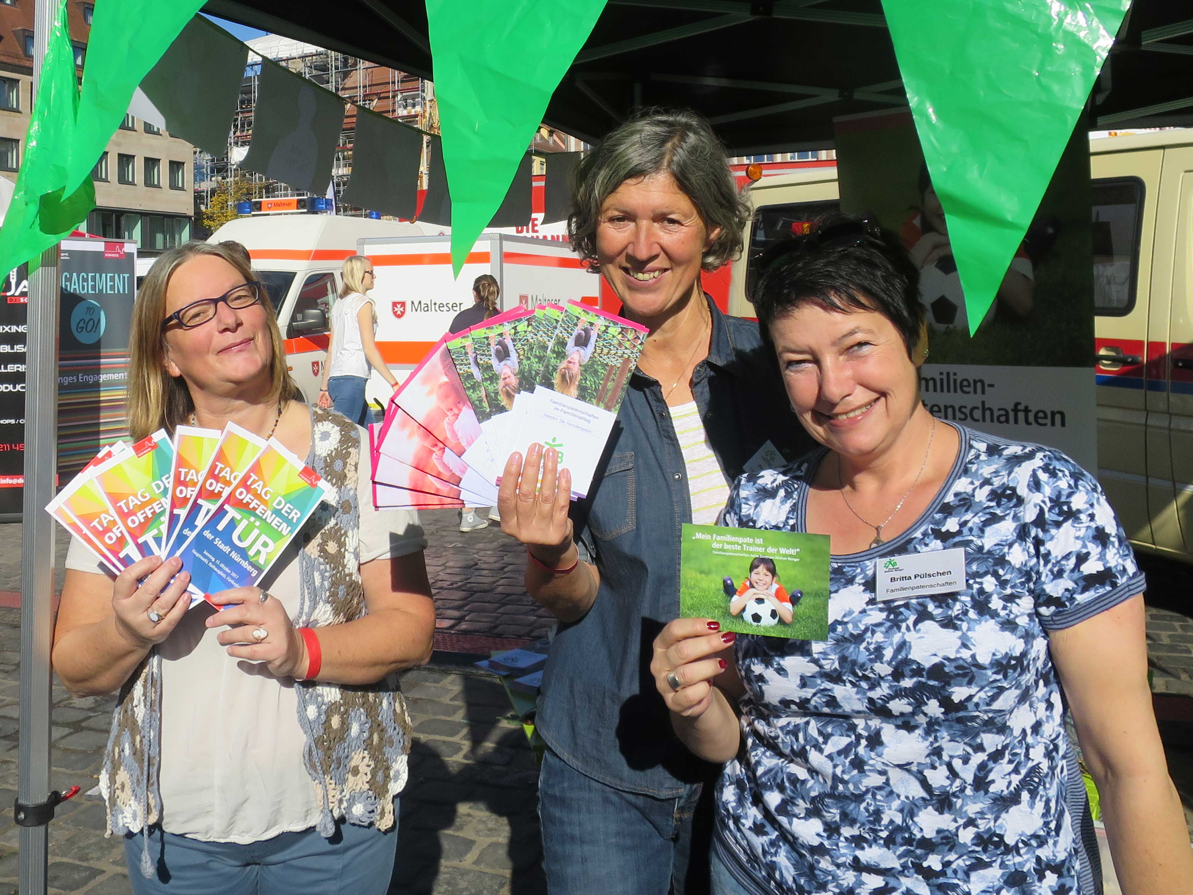 Drei Freiwilligenkoordniatoren mit Flyer in der Hand vor dem Infostand