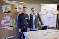 Ein Dozent und eine Dozentin stehen zwischen zwei Pinnwänden mit Moderationskarten.